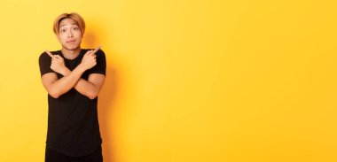 Kararsız yakışıklı adam şaşırmış ve parmaklarını yana doğru gösteriyor, sarı arka planda duruyor..