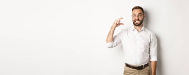 Memnun olmayan sakallı adam küçük bir jest yapıyor, hayal kırıklığına uğramış görünüyor, beyaz arka plana karşı duruyor..