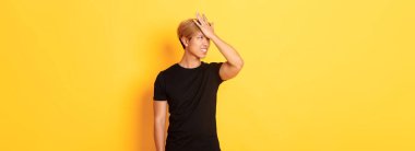 Üzgün ve sorunlu Asyalı adam alnını çatırdatıyor. Unutkan, sarı arka planda duruyor..