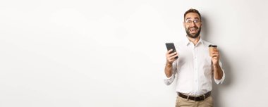 Harika bir iş adamı kahve içiyor, cep telefonuyla harika bir online teklif yapıyor, beyaz arka planda duruyor..
