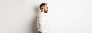 Beyaz yakalı ve bej pantolonlu genç işadamlarının profili, sola bakıyor, stüdyo arka planında duruyor..