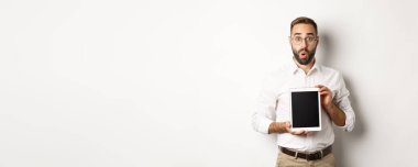 Gözlüklü, dijital tablet ekranı gösteren, şaşırmış, beyaz arka planda duran şaşırmış bir adam..