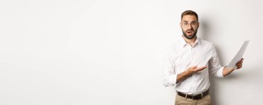 Hayal kırıklığına uğramış patron, kötü rapor için azarlıyor, belgelere işaret ediyor ve kafası karışmış görünüyor, beyaz arka planda duruyor..