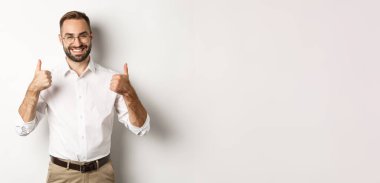 Başarılı iş adamı iyi işi övüyor, başparmaklarını kaldırıyor ve gülümsüyor, beyaz arka planda duruyor..