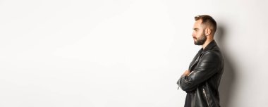 Deri ceketli yakışıklı, ciddi bir adamın profili, sola bakıyor, göğsüne bakıyor özgüvenli, beyaz arka planda..