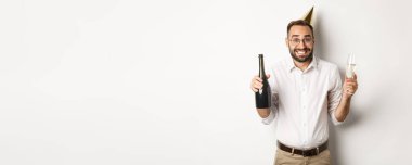 Kutlama ve tatiller. Mutlu yıllar sana, doğum günü partisinin tadını çıkar, komik külah şapka takıp şampanya iç, beyaz arka plan.