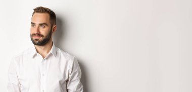 Beyaz gömlekli kendine güvenen işadamlarının yakın çekimi, sola bakıyor ve gülümsüyor, beyaz arka planda duruyor..