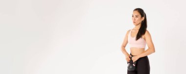 Spor, refah ve aktif yaşam tarzı konsepti. Güçlü odaklı Asyalı kızın yan görünüşü kettlebell ile çömelme hareketleri, fitness egzersizleri sırasında solunum kontrolü, rehabilitasyon egzersizleri....