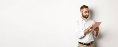 İşadamı dijital tablet üzerinde çalışıyor, meşgul görünüyor, beyaz arka planda duruyor..