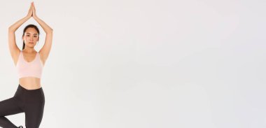 Spor, spor salonu ve sağlıklı vücut konsepti. Tam boy odaklanmış, ince esmer Asyalı kız fitness kıyafetleri üzerinde yoga yapıyor. Kız kollarını kaldırıyor ve Asana pozunda duruyor, beyaz arkaplan.