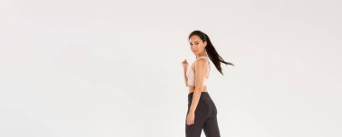 Şımarık, yakışıklı, spor yapan ince Asyalı kız, sporcu ya da antrenman koçu kendinden emin, motive olmuş bir ifadeyle yürüyen, kameraya dön lütfen gülümse, beyaz arka plan.