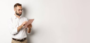 İşadamı dijital tablet üzerinde çalışıyor, meşgul görünüyor, beyaz arka planda duruyor..