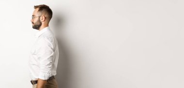 Beyaz yakalı ve bej pantolonlu genç işadamlarının profili, sola bakıyor, stüdyo arka planında duruyor..