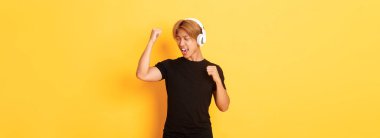 Kaygısız, çekici, sarı saçlı, şarkı söyleyen ve dans eden, kablosuz kulaklıkla müzik dinleyen, sarı arka planda duran Asyalı adam..