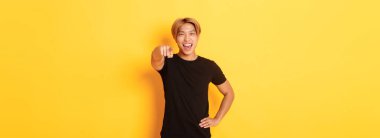 Sarı saçlı, neşeli ve yakışıklı Asyalı bir adamın portresi. Seni seçiyor, gülümsüyor ve kamerayı işaret ediyor. Tebrikler..