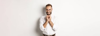 Genç kurnaz işadamı parmaklarını çırpıyor ve gülümsüyor. Sinsi, entrikacı plan, beyaz arka planda duruyor..