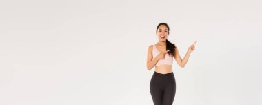 Tam boy arsız çekici bayan sporcu, spor giyimli Asyalı fitness kızı sağ üst köşeyi işaret ediyor, tanıtım yapıyor, egzersiz malzemeleri satışı, fitness eğitimi indirimi gösteriyor..