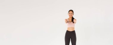 Gülümseyen, yakışıklı ve ince Asyalı fitness koçu aktif giyimli bayan sporcu egzersiz ekipmanları gösteriyor, direnç bandı tutuyor, egzersiz yapıyor, beyaz arka plan.