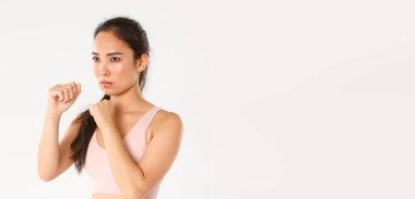 Spor, refah ve aktif yaşam tarzı konsepti. Spor kıyafetli, sıkı yumruklar sallayan, somurtan, kendini savunma kurslarına giden, gölgeli boks yapan ciddi Asyalı bir kızın yan görüntüsü..