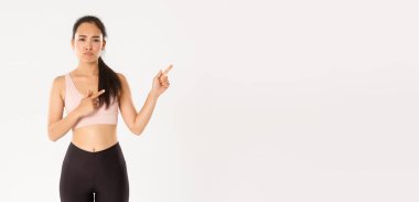 Spor, refah ve aktif yaşam tarzı konsepti. Hüzünlü Asyalı kız üzgün görünüyor, sporcu kadın ya da spor salonu müşterisi somurtkan suratıyla sağ üst köşeyi gösteriyor, şikayet ediyor..