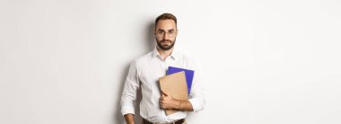 Yakışıklı erkek çalışanın elinde defterler var, kendinden emin görünüyor, beyaz arka planda duruyor..