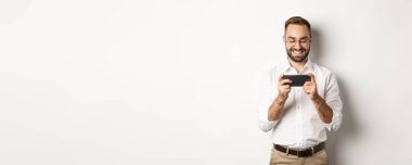 Mutlu iş adamı cep telefonundan video izliyor, beyaz arka planda duruyor..