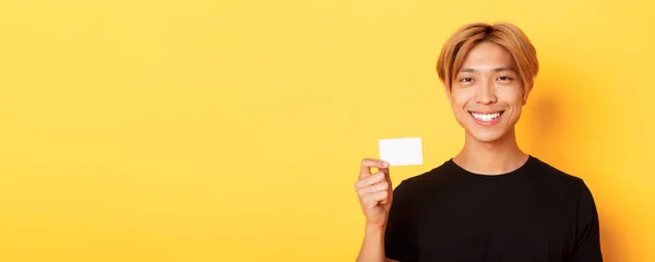 閉じるアップのハンサムな喜びアジアの男とともにフェア髪 笑顔幸せとショークレジットカード上の黄色の背景 — ストック写真