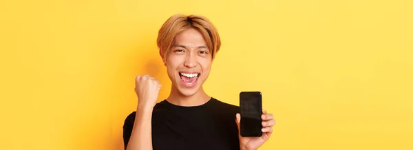 Zbliżenie Szczęśliwego Radującego Się Azjatyckiego Faceta Pokazującego Ekran Smartfona Mówiącego — Zdjęcie stockowe
