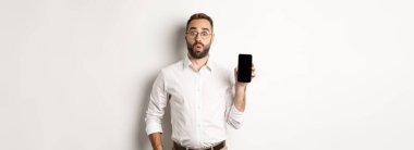 Gözlüklü yakışıklı yönetici, meraklı görünüyor ve ekranı gösteriyor, beyaz arka planda duruyor..