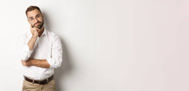 Kameraya hoşnutsuz bakan, beyaz arka planda karamsar duran, gözlüklü, komik olmayan sakallı adam..