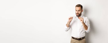 Gözlüklerine bakan, beyaz arka planda ofis kıyafetleri giyen bir adam..