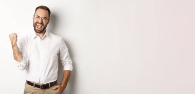 Başarılı iş adamı seviniyor, yumruk tokuşturuyor ve evet diyor, hedefine ulaşıyor, beyaz arka planda duruyor..