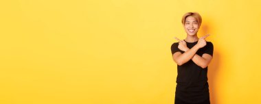 Yakışıklı, kararlı, sarışın Asyalı bir adamın portresi. Öğrenci iki farklı türü gösteriyor. Sarı arka planda duruyor..