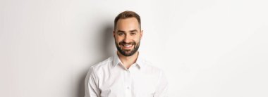 Beyaz yakalı, kendine güvenen, kameraya gülümseyen, stüdyo arka planına karşı kendinden emin bir erkek çalışanın yakın çekimi..