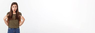 Gri arka planda yalnız duran mutlu ve şaşırmış genç bir bayan portresi. Kamera işaret ediyor