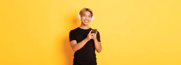 Добре Виглядає Усміхнений Задоволений Азіатський Хлопець Бездротових Навушниках Тримає Смартфон — стокове фото