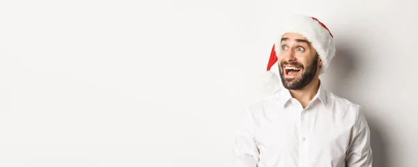 サンタの帽子の驚くべき髭の男のクローズアップは 興奮して左を見て クリスマスプロモーションオファー 白い背景の上に立って — ストック写真