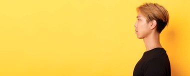 Yakışıklı, stil sahibi Koreli bir adamın profil fotoğrafı ciddi bir ifadeyle sol tarafa bakıyor, sarı arka planda duruyor..