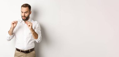 Gözlüklerine bakan, beyaz arka planda ofis kıyafetleri giyen bir adam..