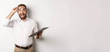 Etkileyici yönetici elinde pano, kameraya bakıyor, beyaz arka planda duruyor..