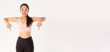Spor, refah ve aktif yaşam tarzı konsepti. Heyecanlı ve mutlu Asyalı spor giyim kızı, parmakları aşağıda ve büyük indirimlerle şaşkın bakıyor, afiş okuyor, beyaz arka plan.