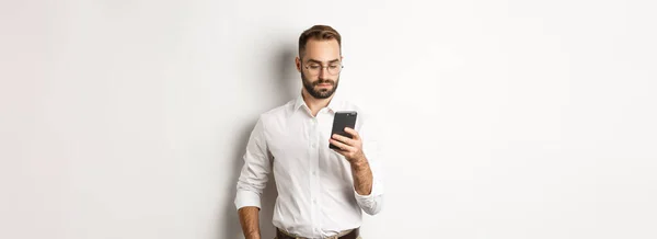 ビジネスマンは白い背景の上に立って電話でメッセージを読む — ストック写真