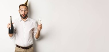 Kutlama ve tatiller. Şaşkınlık içinde, elinde şampanya ve cam tutan, beyaz arka planda duran, sürpriz bir adam..