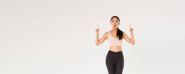 Afallamış ve etkilenmiş Asyalı kadın sporcu, spor giyimli kadın heyecanlı yüzüyle parmaklarını havaya kaldırıyor. Fitness kızı spor mağazasında özel bir teklifle merak etti..