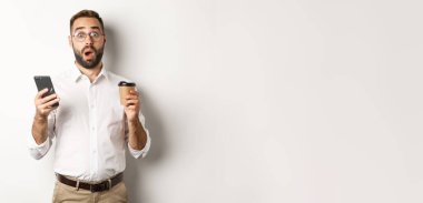 Yakışıklı adam kahve içmeyi başarıyor, cep telefonundan gelen mesaja şaşırıyor, beyaz arka planda duruyor..