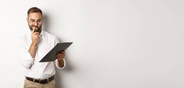 Düşünceli bir çalışan panoya bakıyor, şüpheleri var, beyaz arka planda duruyor..