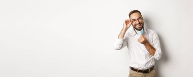 Covid-19, sosyal uzaklık ve karantina konsepti. Mutlu iş adamı maskesini çıkar ve gülümse, beyaz arka planda dur..