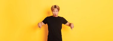 Şaşırmış Asyalı adamın portresi şaşırmış, parmaklarını göstermiş ve sarı arka planda duran pankarta bakıyordu..