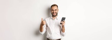 Memnun olmuş bir iş adamı cep telefonu kullandıktan sonra beyaz arka planda mutlu mesut duruyor..