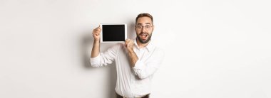 Alışveriş ve teknoloji. Yakışıklı adam dijital tablet ekranı gösteriyor, beyaz yakalı gözlük takıyor, stüdyo geçmişi var..